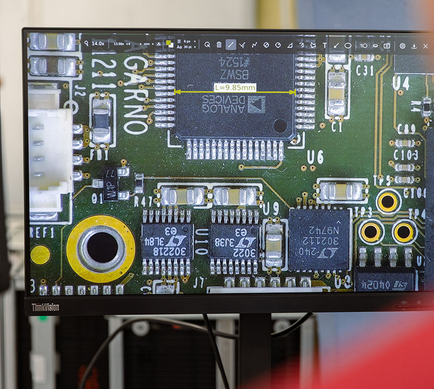 Monitor showing a magnified PCB with a measuring software on top measuring the length of a component